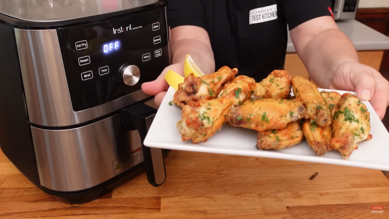 man holding a bowl with chicken wings - air fryer on the left side near him