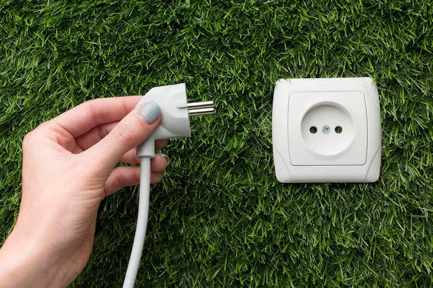 Hand holding a plug, ready to insert it into a socket on a green grass wall