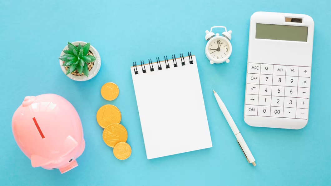 Calculator, notepad, coins, and a piggy bank on a table